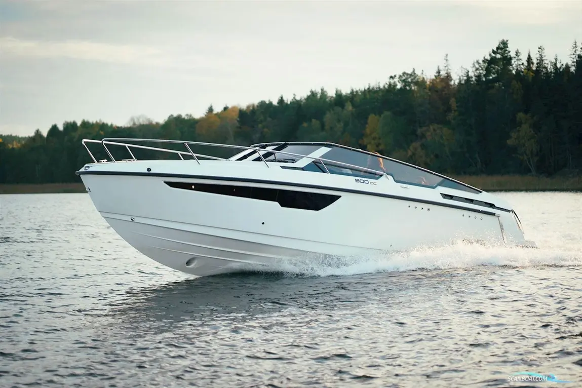 A sleek white motorboat, model 900 DC, glides through calm water with a scenic forest backdrop.